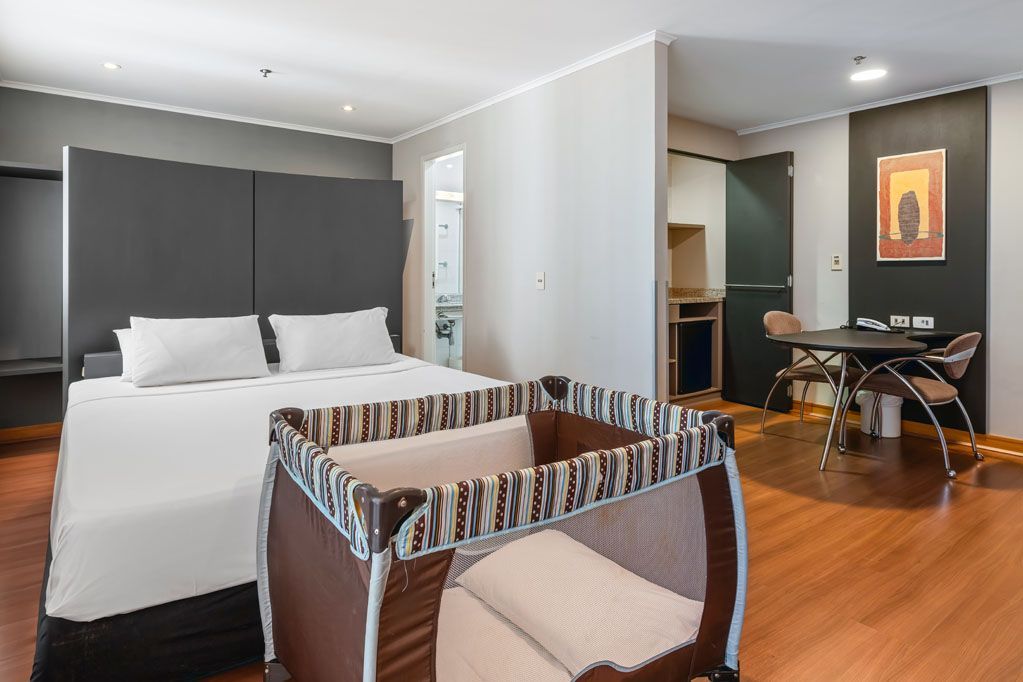 Quarto de hotel moderno com cama, berço, escrivaninha e paredes cinza.