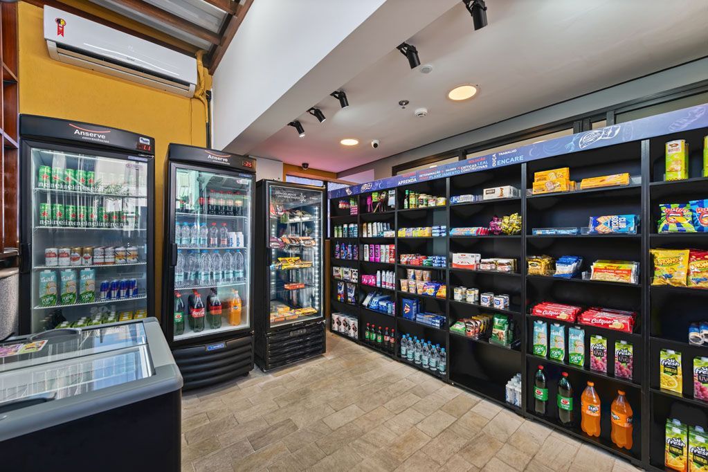 Corredor de loja de conveniência com refrigeradores e prateleiras abastecidas com lanches e bebidas.