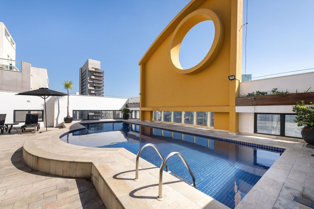 Piscina na cobertura com água azul, deck curvo e uma parede amarela com uma grande abertura circular.
