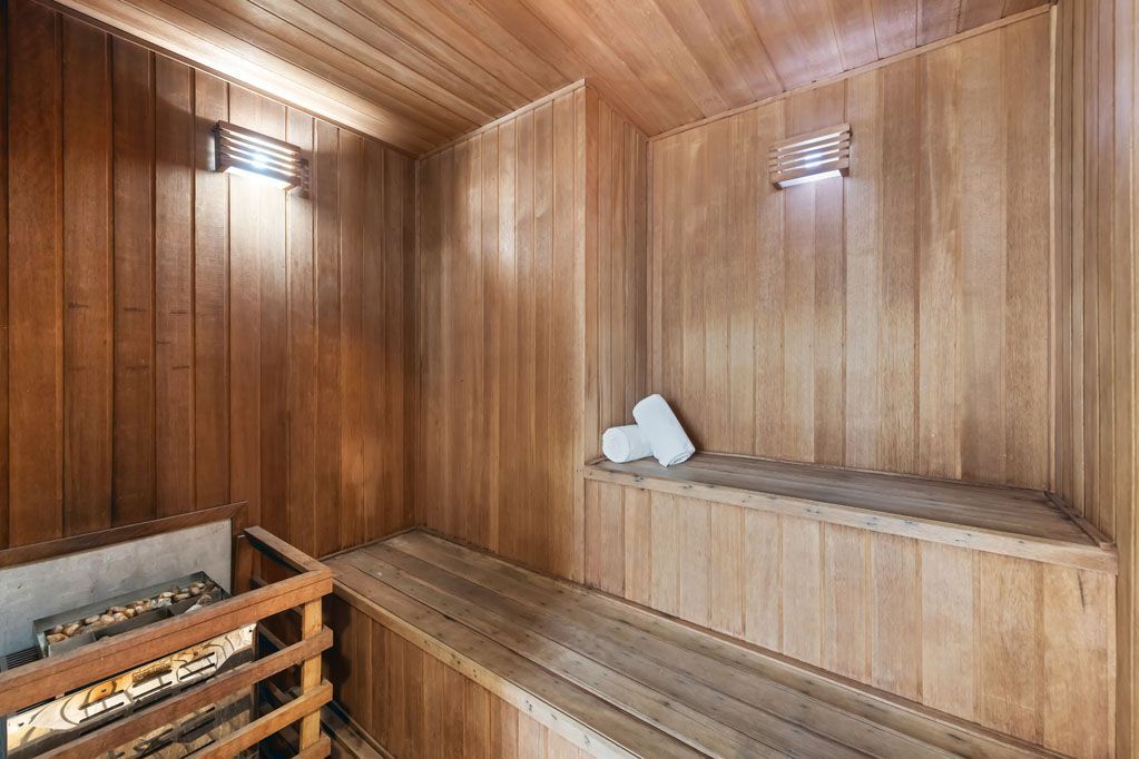 Sauna com painéis de madeira, bancos e aquecedor, iluminada por luminárias de parede.