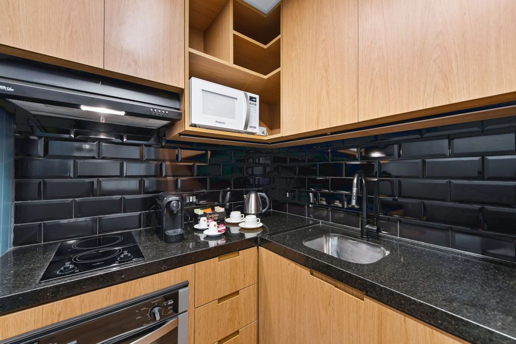 Cozinha moderna de canto com backsplash de azulejos pretos, armários de madeira e bancadas de granito escuro.