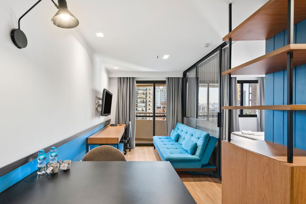 Sala de estar moderna e estreita com sofá azul, mesa de jantar, estantes de madeira e portas para a varanda.