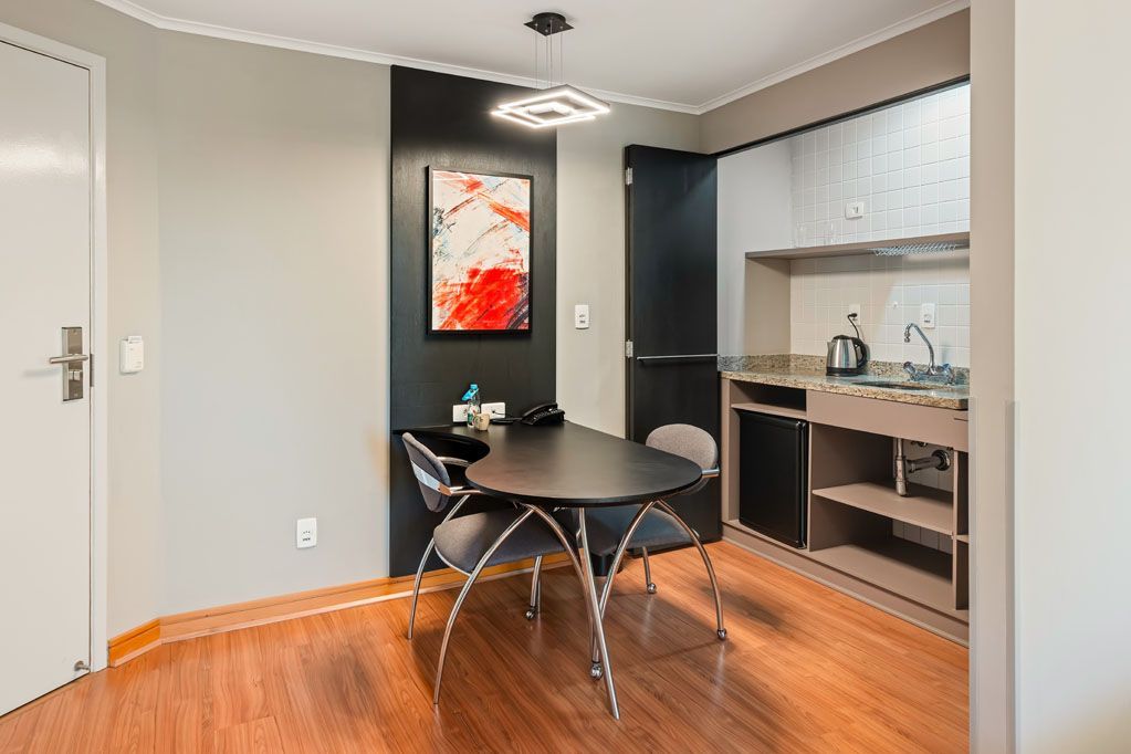 Sala de jantar moderna com mesa preta, cadeiras de metal, balcão americano para a cozinha e obras de arte emolduradas na parede.