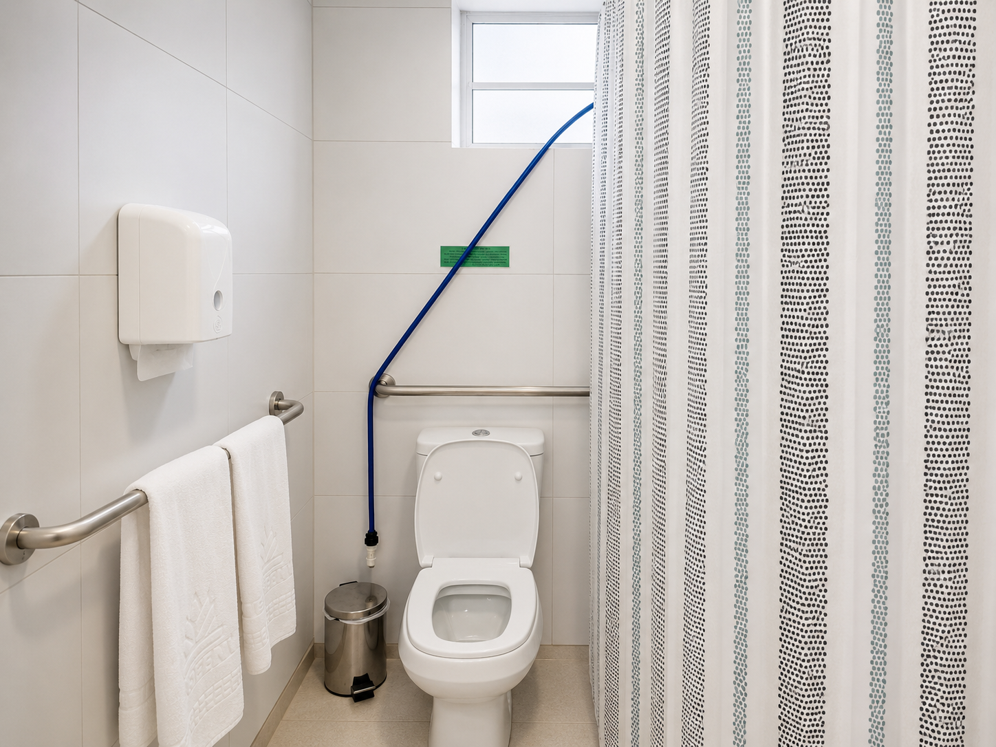 Banheiro acessível com vaso sanitário, barras de apoio, suporte para toalhas e corda de suporte azul perto do vaso sanitário.