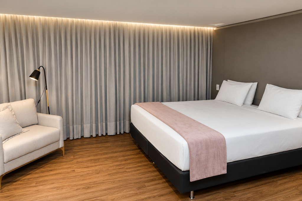 Quarto de hotel moderno com cama grande, poltrona e cortinas do chão ao teto em um ambiente de tons quentes.