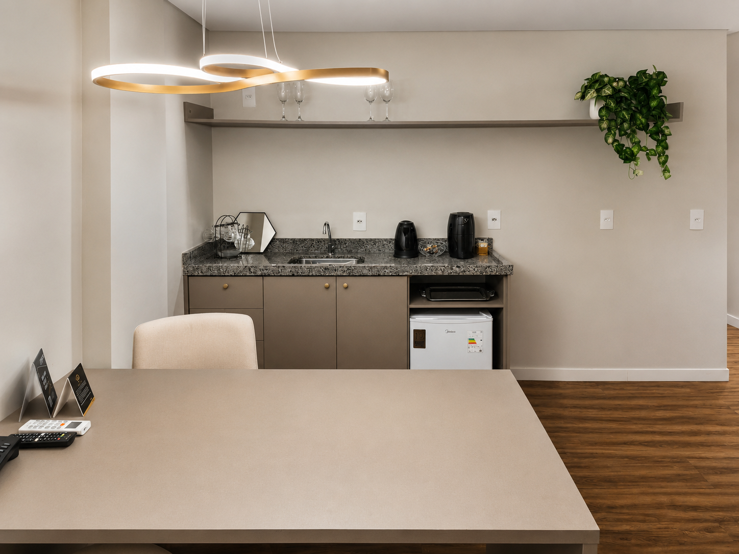 Cozinha e sala de jantar modernas com mesa bege, armários cinza, piso de madeira e luminárias pendentes.