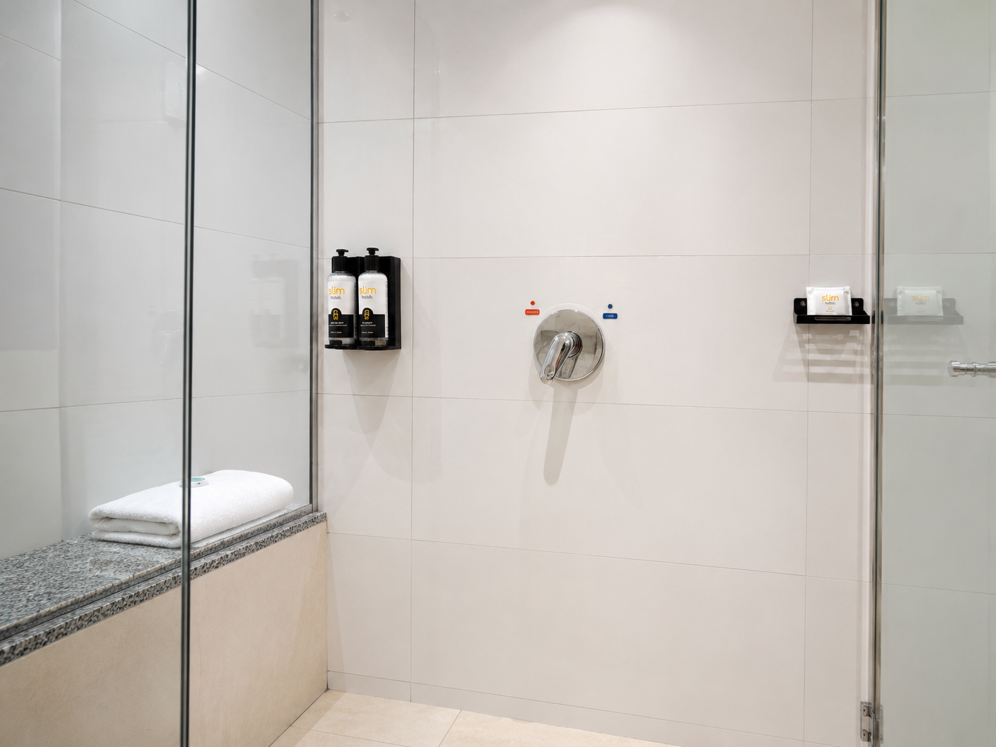 Chuveiro moderno com divisória de vidro, azulejos bege e dispenser de produtos de higiene pessoal embutido.