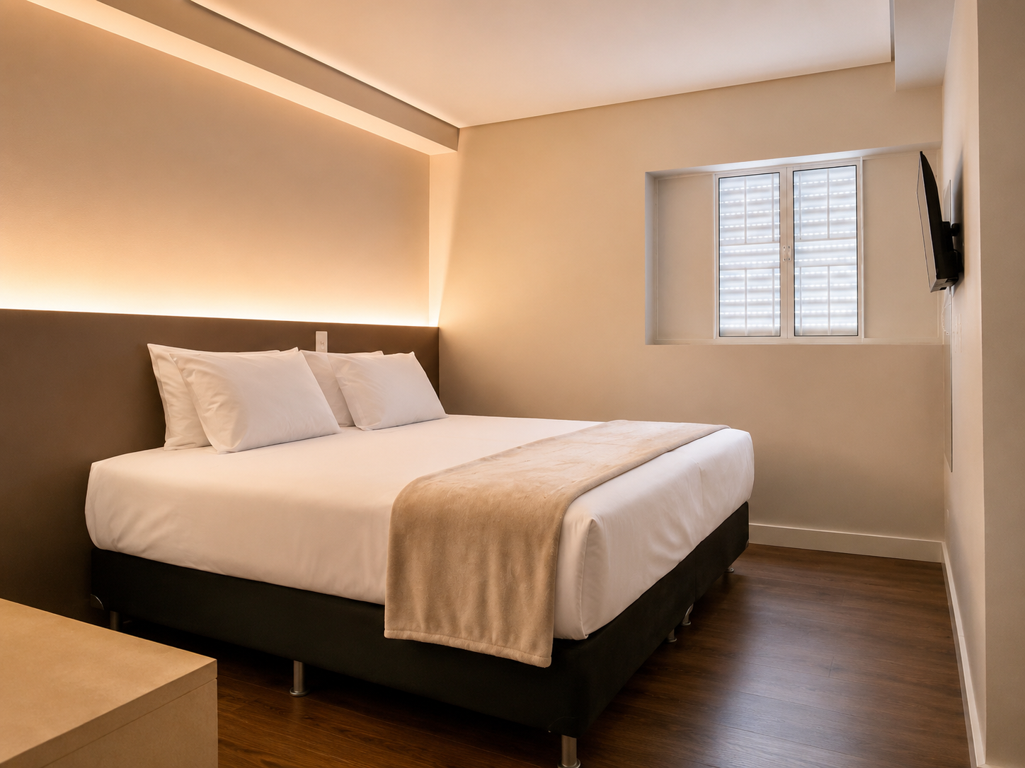 Quarto moderno com uma cama grande, iluminação ambiente aconchegante, piso de madeira e uma pequena janela.