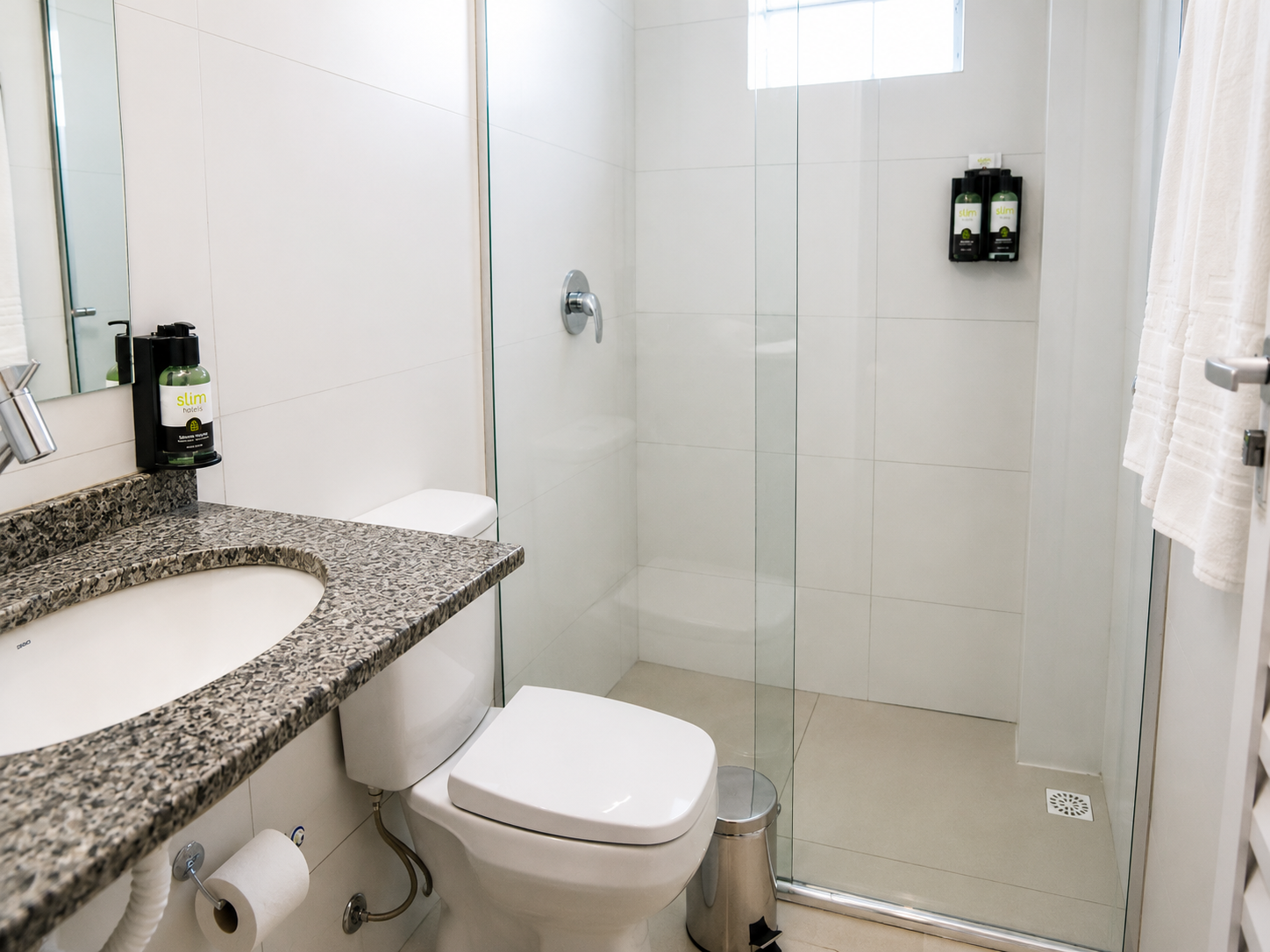 Banheiro pequeno e moderno com pia, vaso sanitário e box de vidro em tons de branco e cinza.