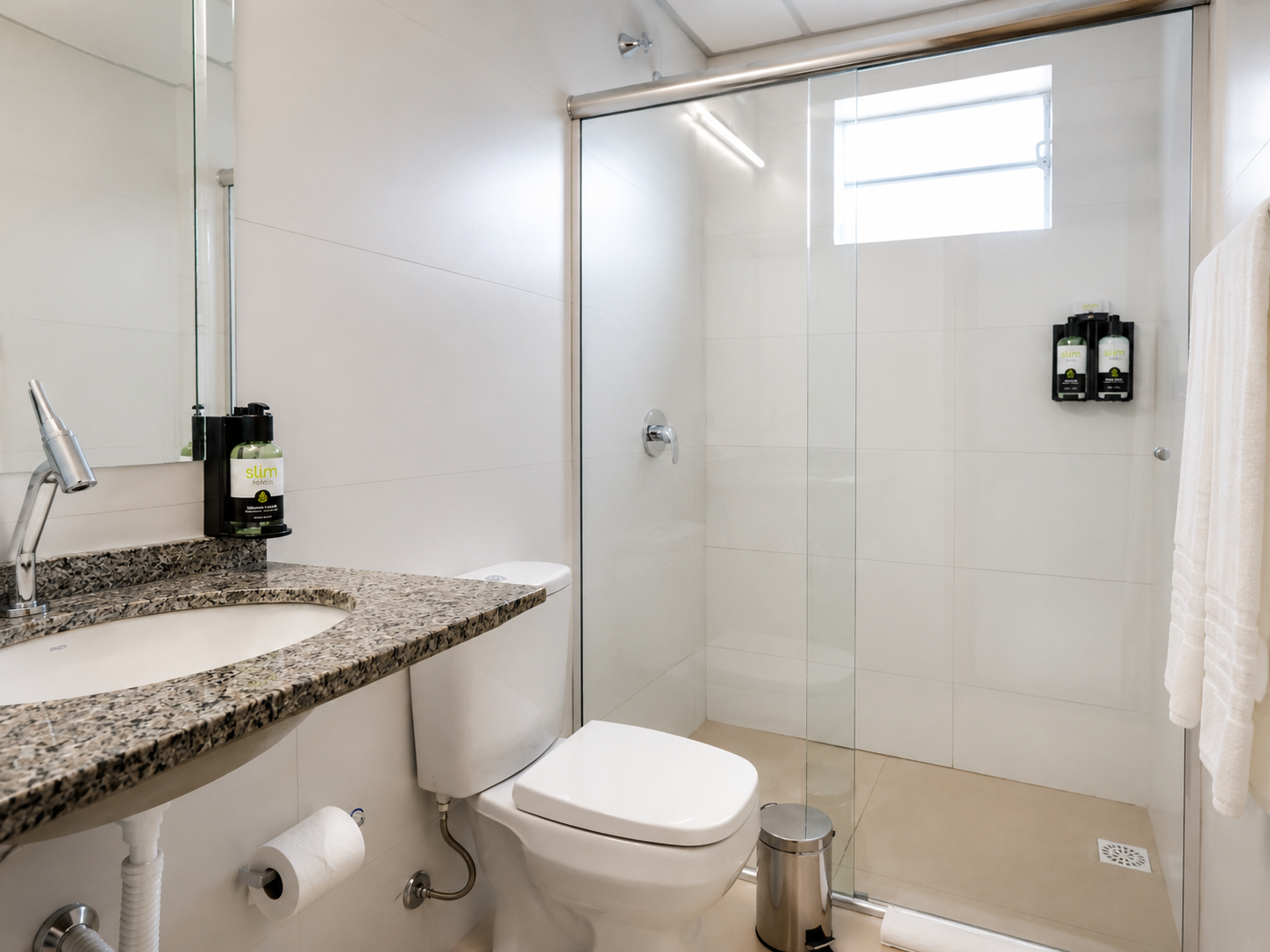 Banheiro moderno com pia de granito, vaso sanitário suspenso, box de vidro e paredes revestidas com azulejos brancos.