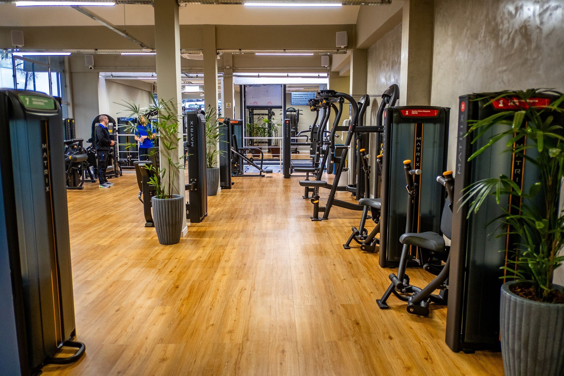 Interior de academia moderna com piso de madeira, aparelhos de ginástica e espelhos.