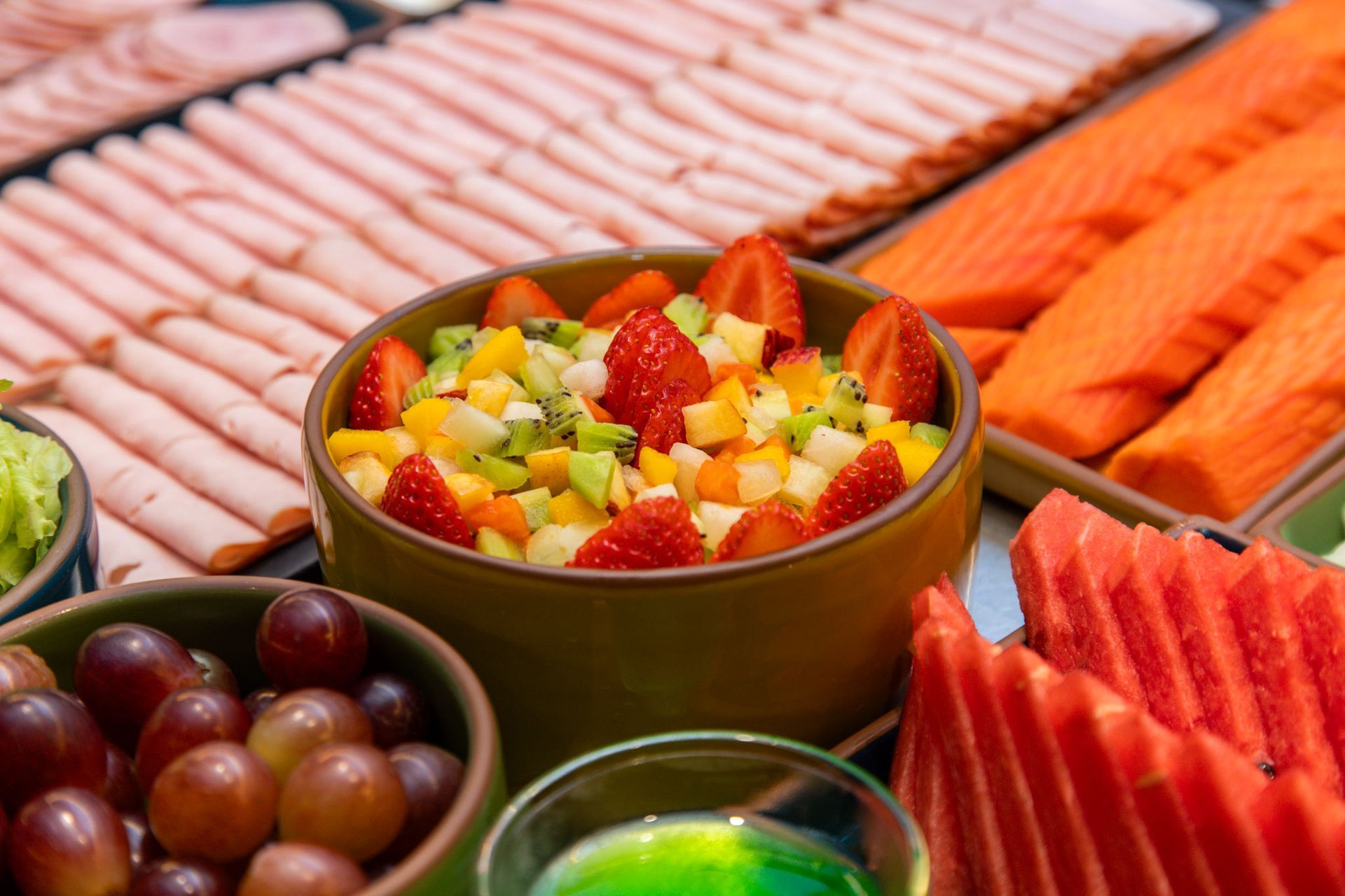 Buffet de frutas frescas com morangos, uvas, cubos de melão e fatias de melancia em uma mesa colorida.