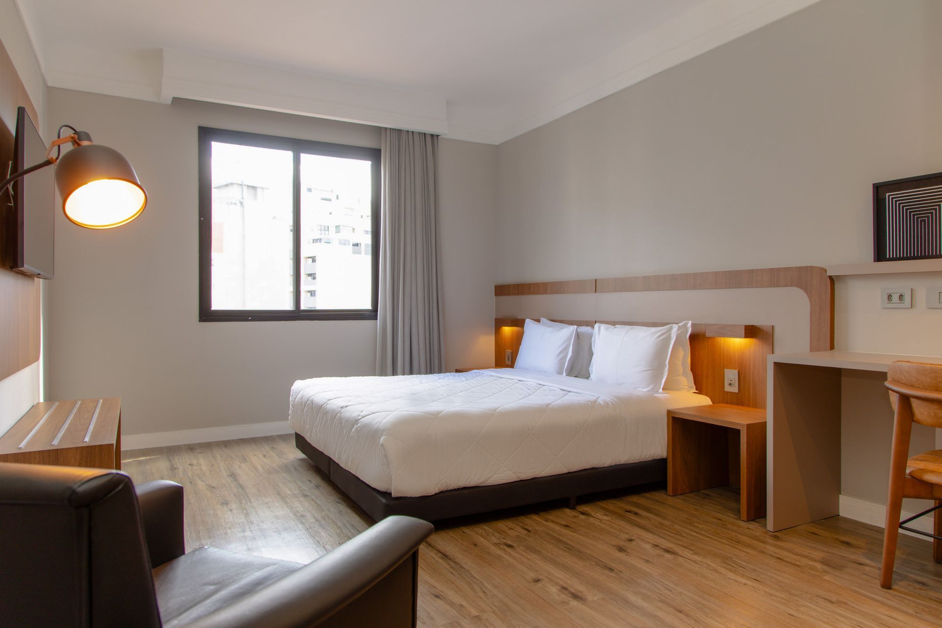 Quarto moderno com cama, escrivaninha, cadeira, luminária de chão e janela com cortinas cinza.
