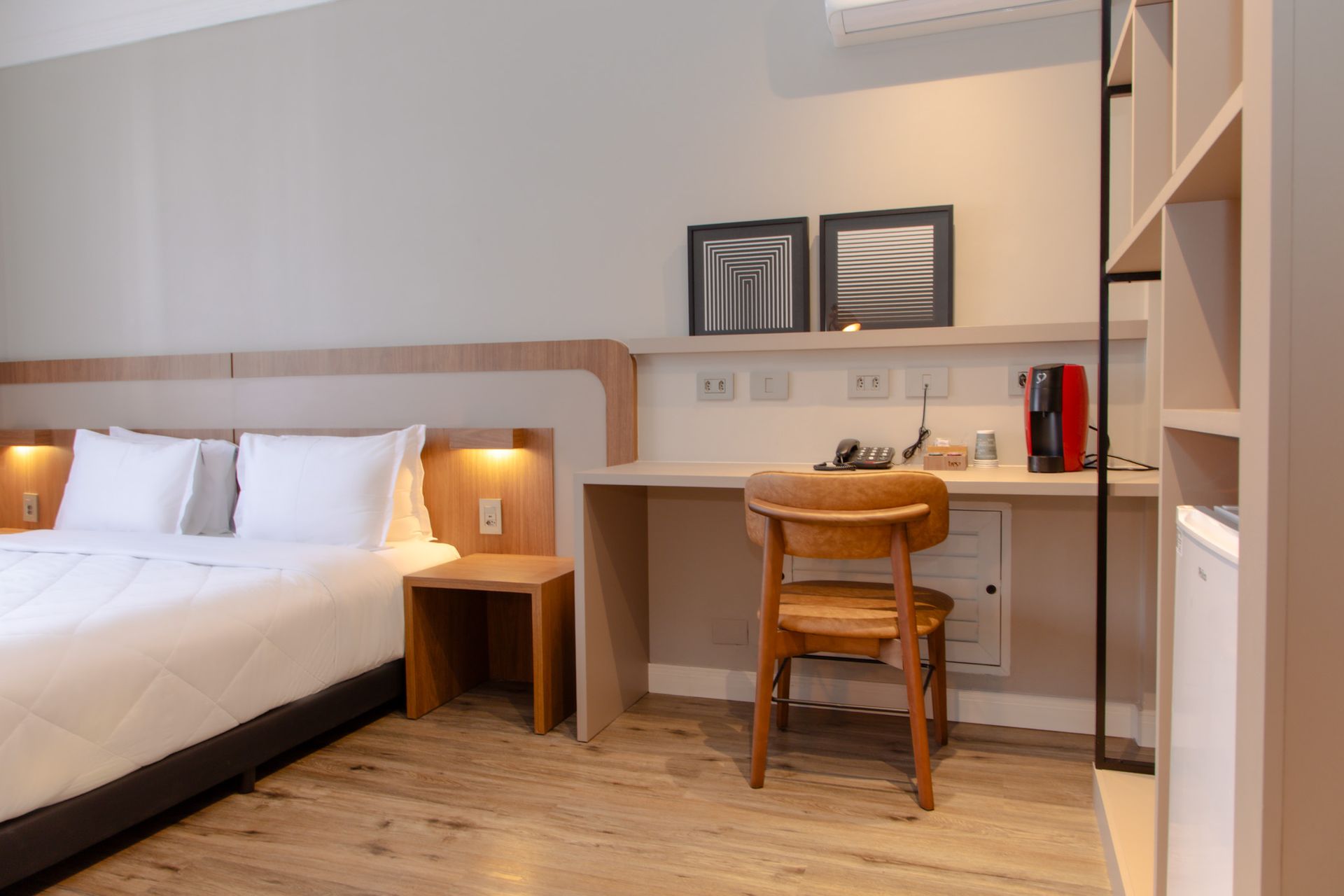 Quarto de hotel moderno com cama, escrivaninha, cadeira de madeira e abajures aconchegantes.