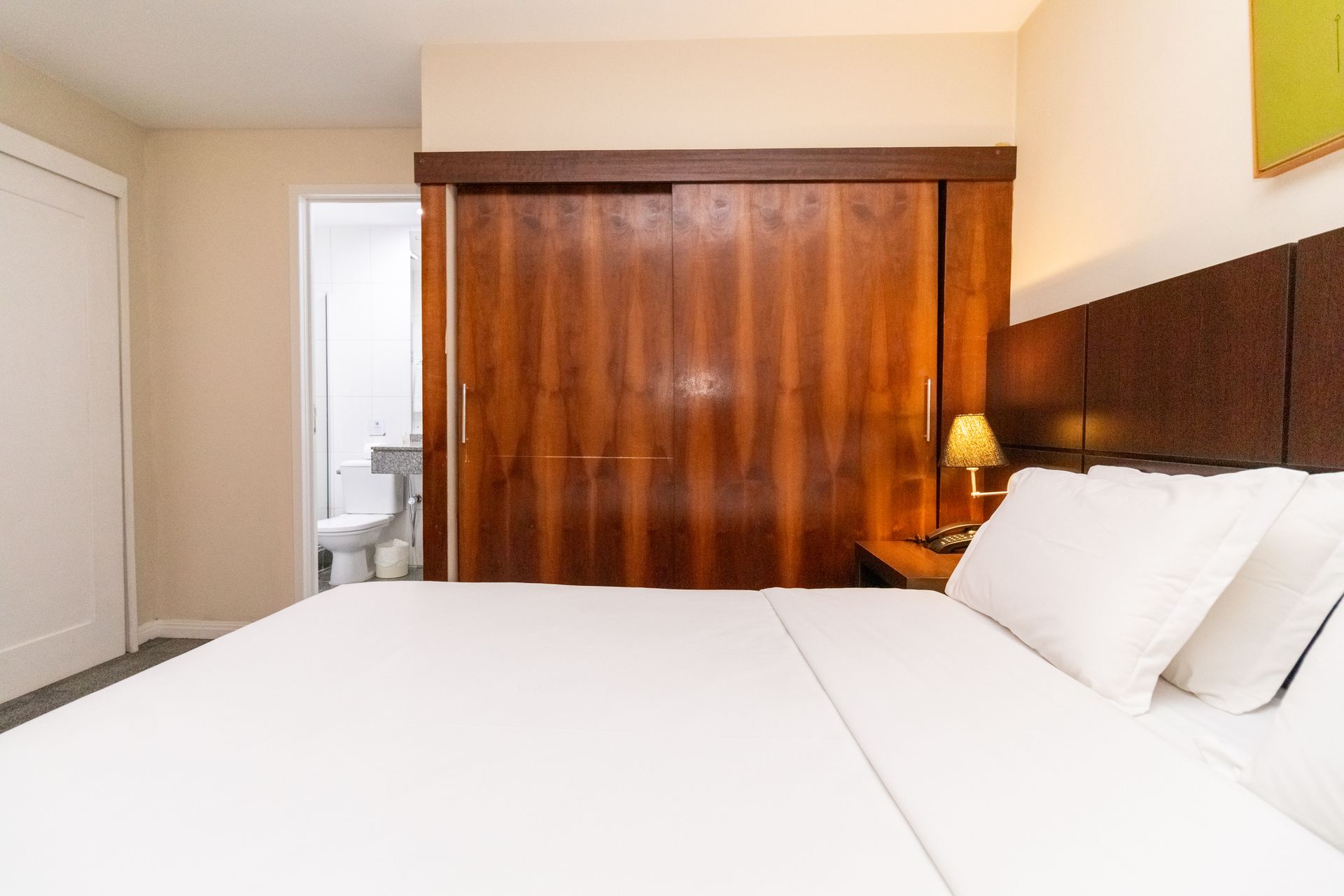 Quarto moderno com cama grande, guarda-roupa de madeira com portas de correr e um abajur aconchegante.