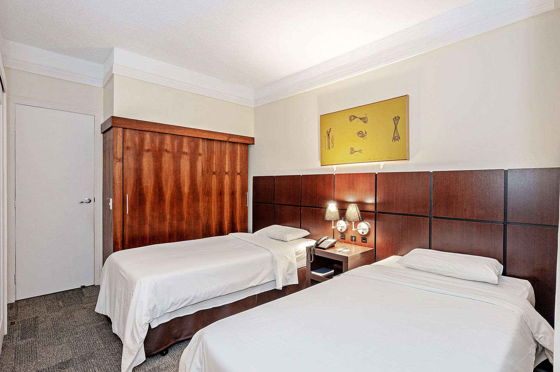 Quarto de hotel com duas camas, cabeceira marrom, cortina laranja e abajures.
