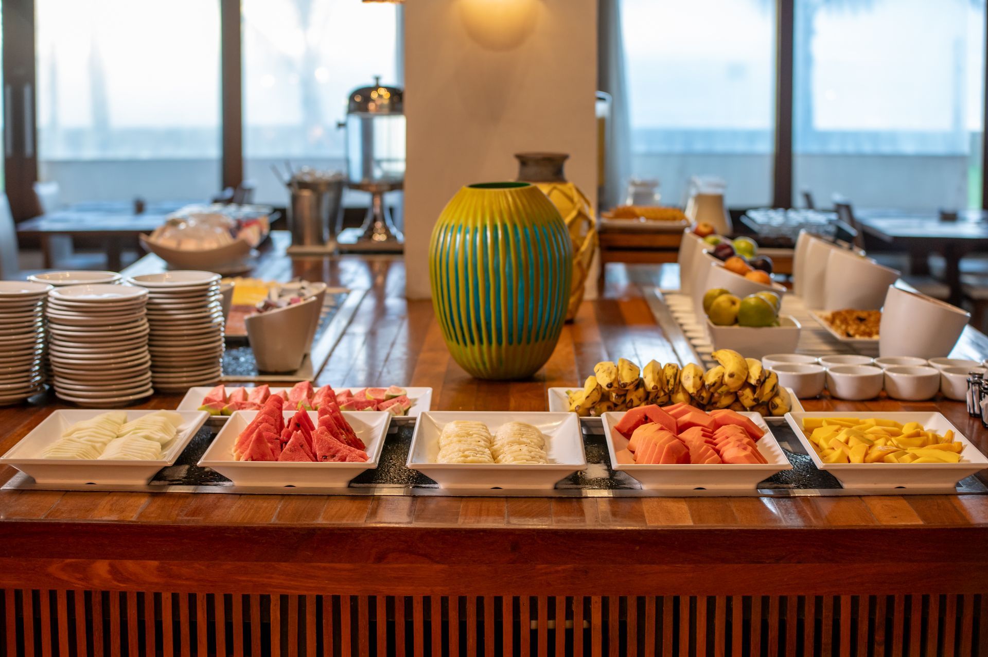 Buffet de café da manhã com frutas, doces e tigelas de cereais em um balcão de madeira na sala de jantar.