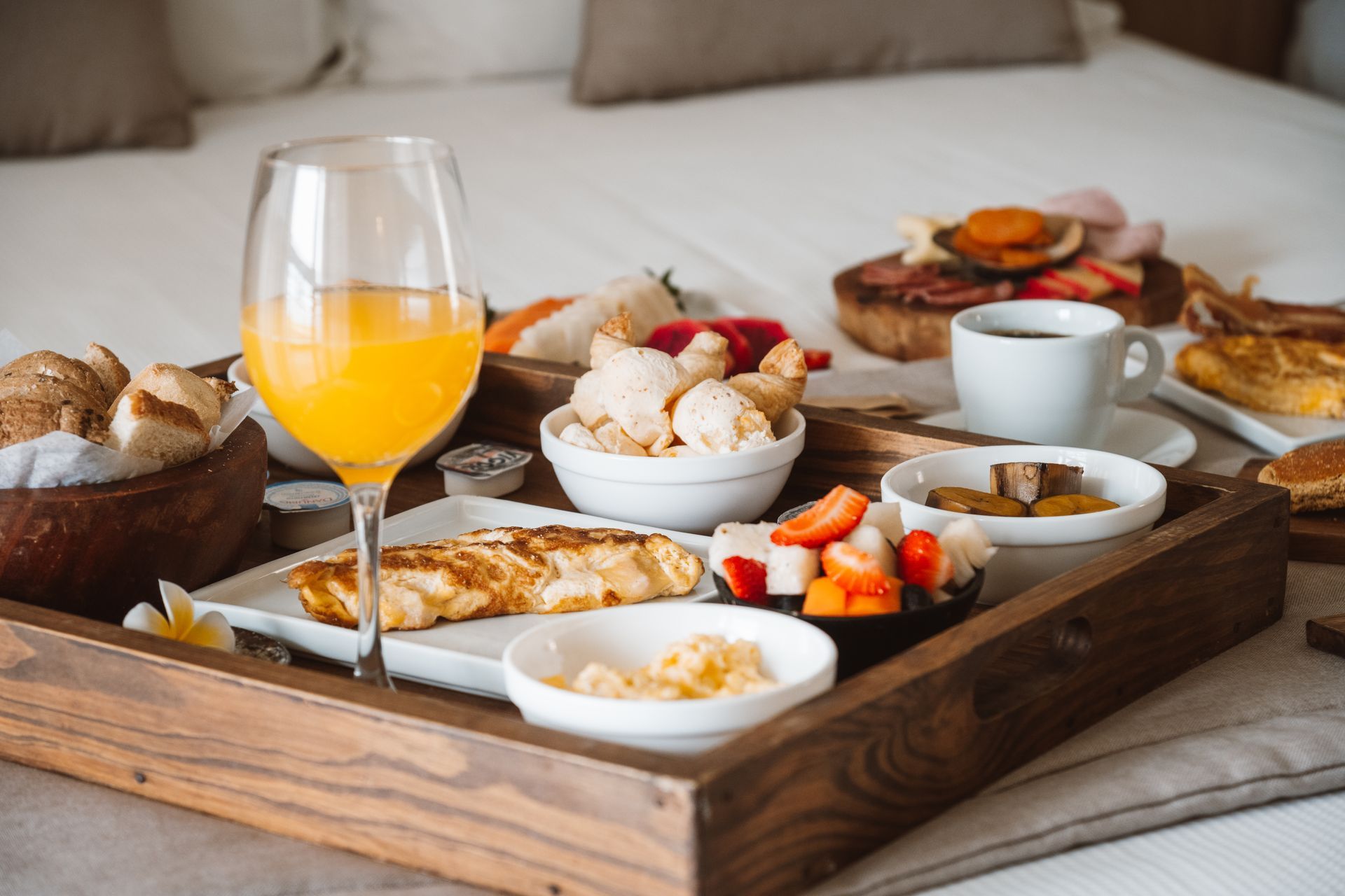 Bandeja de café da manhã na cama com suco de laranja, doces, frutas e xícaras de café.
