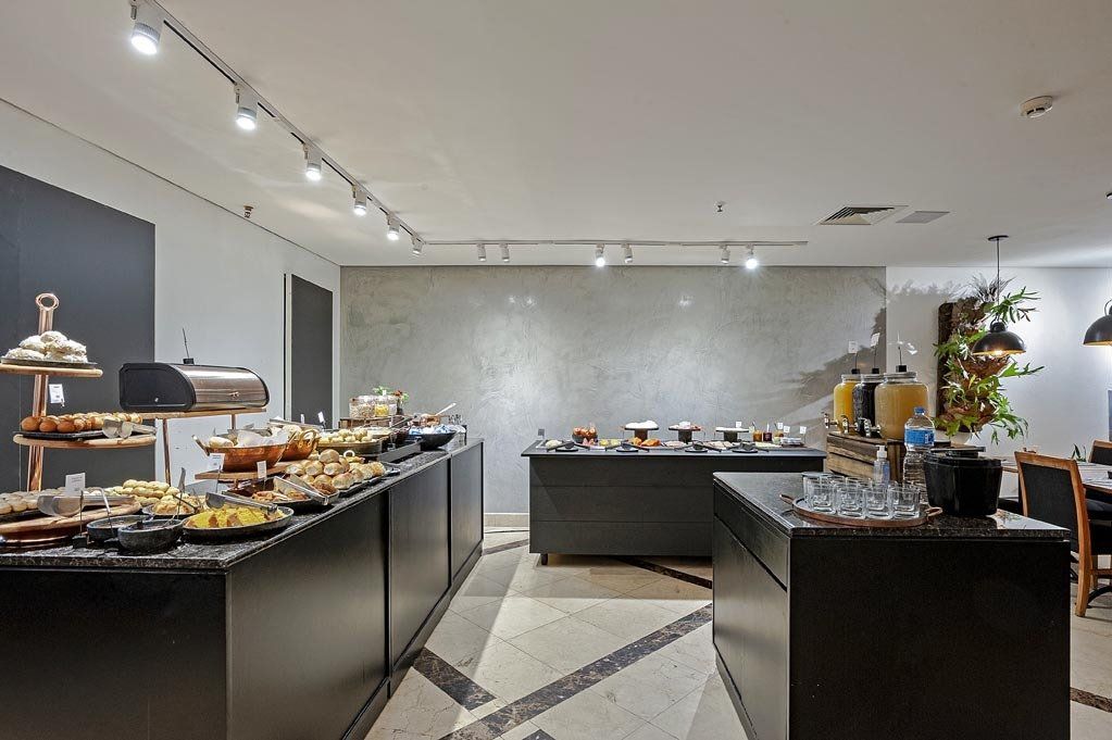 Buffet moderno com mesas pretas, pratos servidos à mesa e uma parede prateada em um ambiente iluminado.
