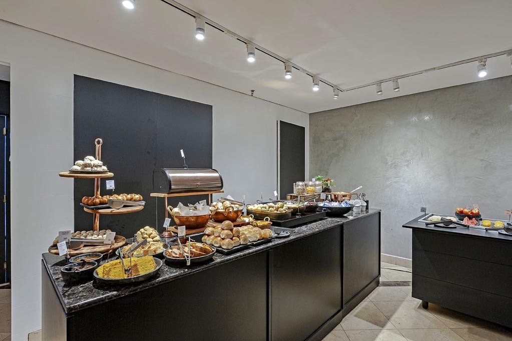 Buffet disposto sobre mesas pretas em uma sala de jantar moderna e iluminada com iluminação direcionada.
