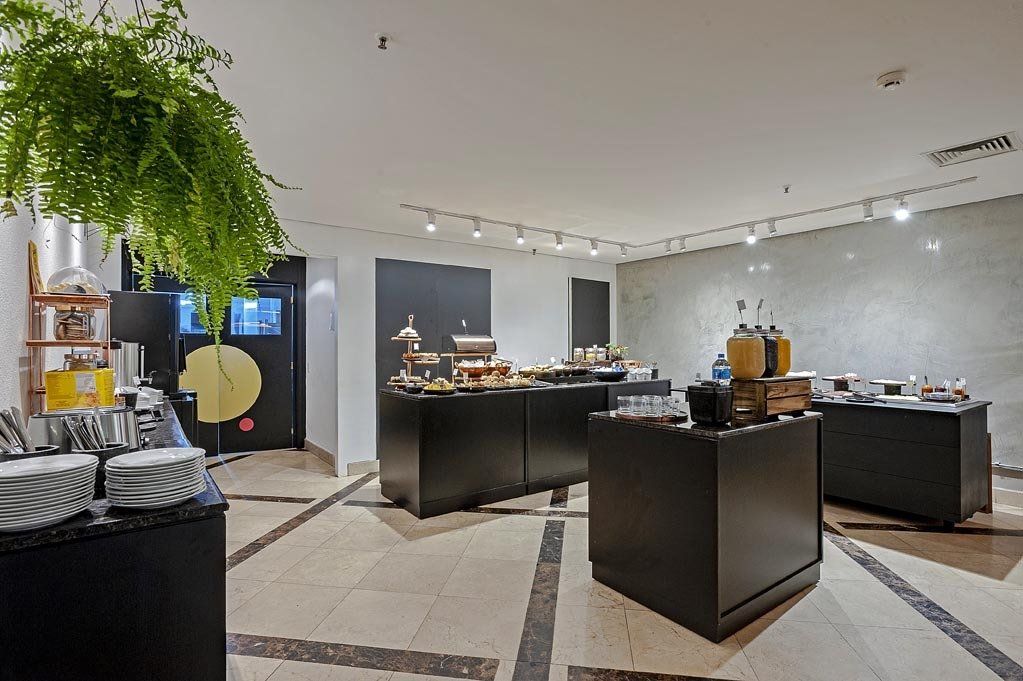 Exibição de buffet moderno em uma sala clara e elegante com mesas pretas e plantas suspensas.