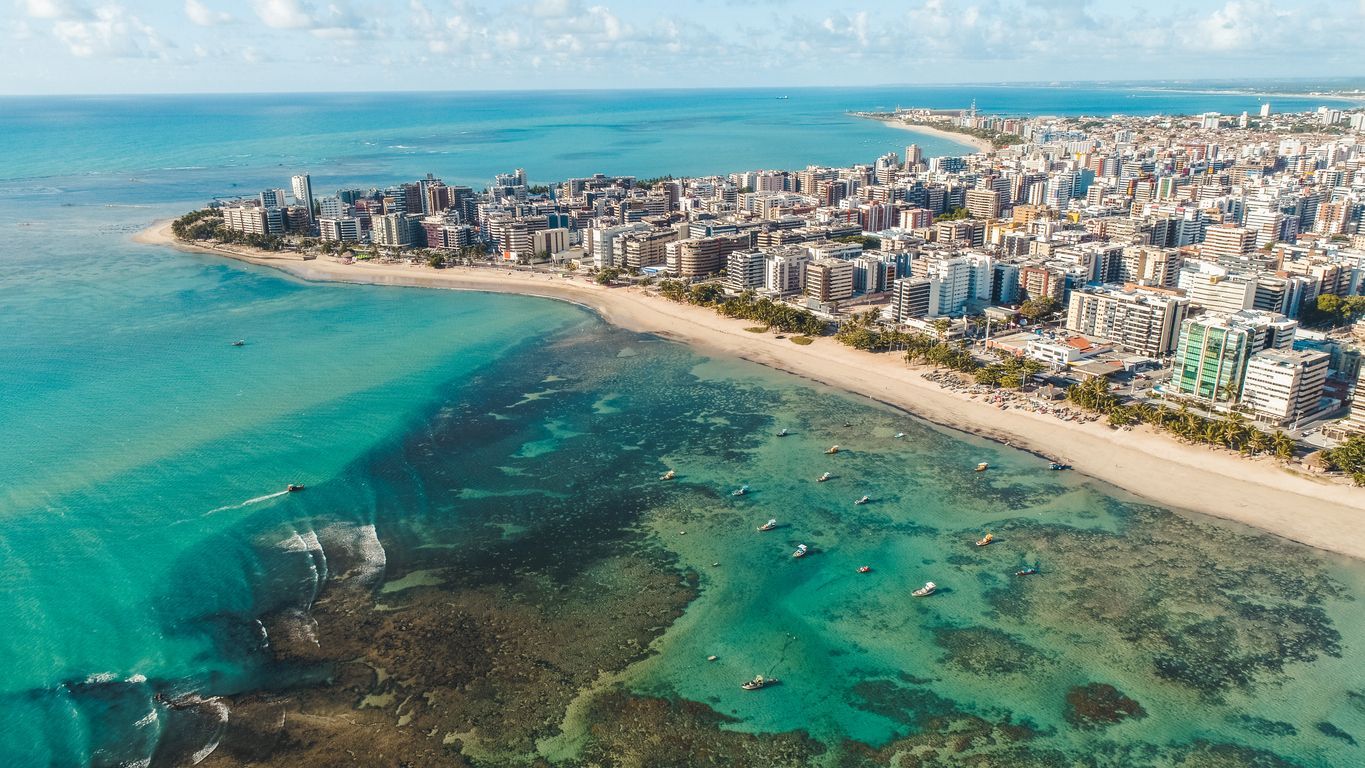 Vista aérea de uma cidade costeira com muitos arranha-céus, uma praia de areia e águas turquesas que contornam a costa.