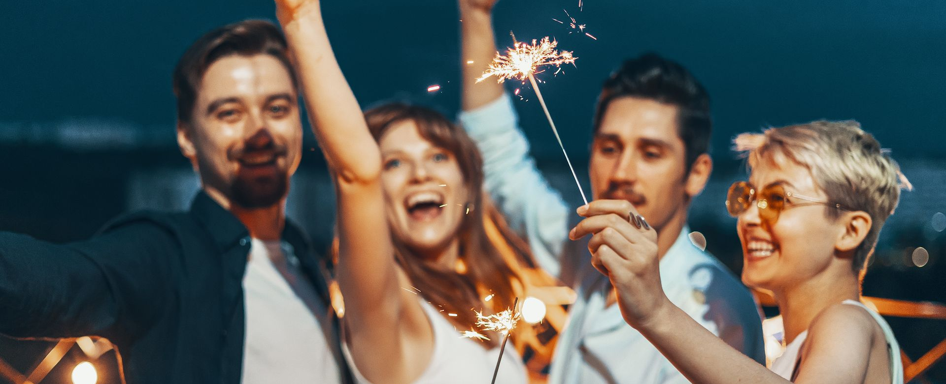 Amigos sorrindo e segurando velas de faísca em uma festa noturna festiva.