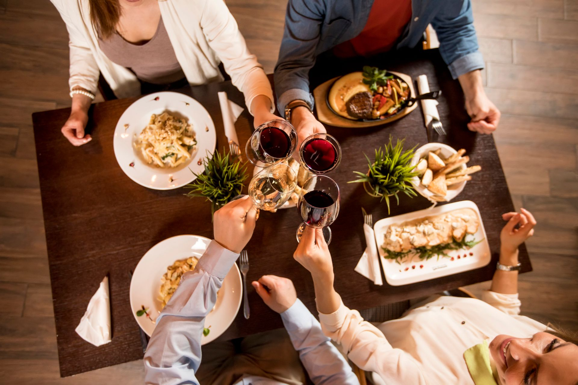 Amigos brindam com taças de vinho em uma mesa de jantar compartilhada, com pratos, salada e pão.