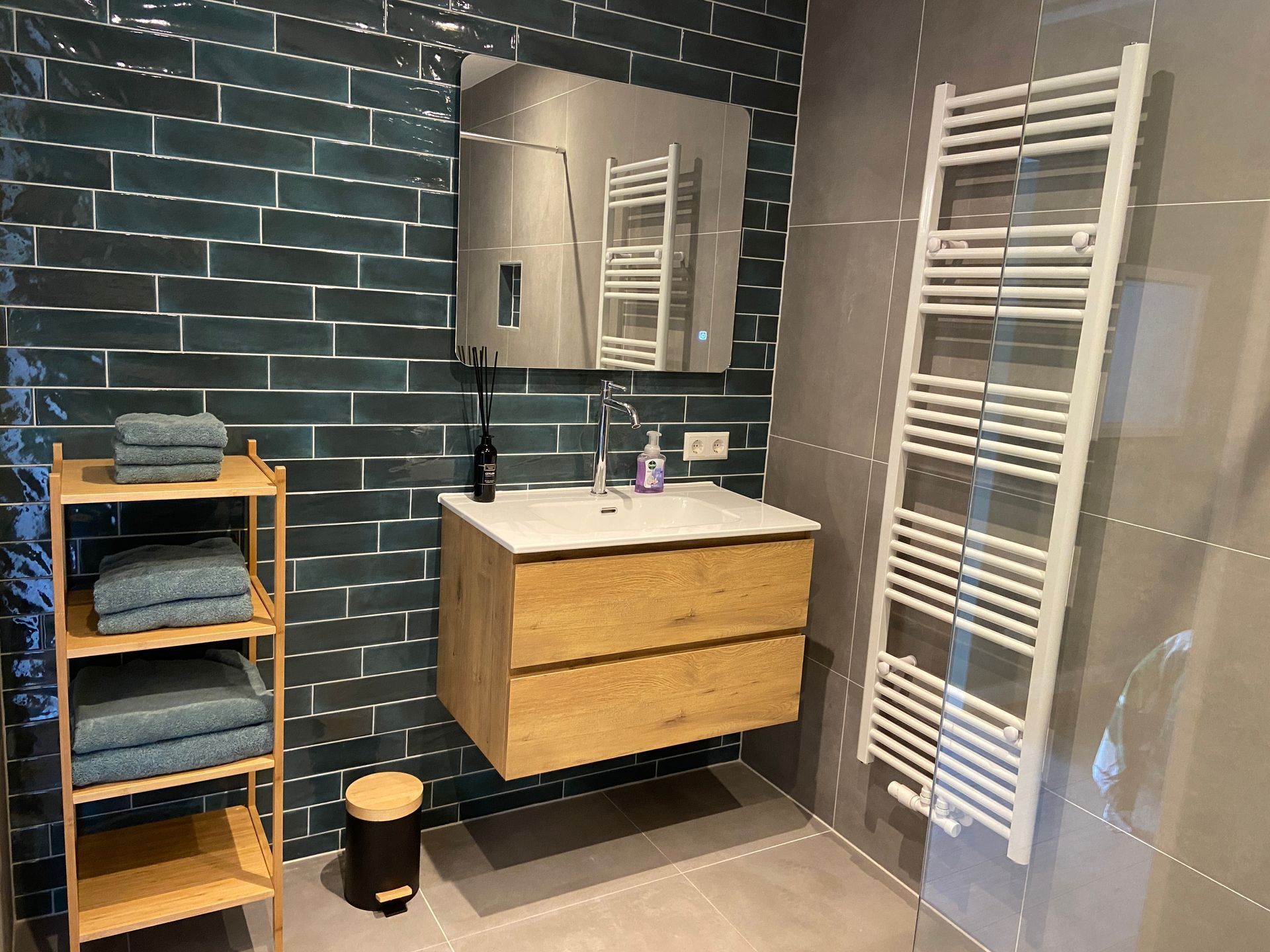 Moderne badkamer met groene tegelwanden, zwevend houten badmeubel, staand handdoekenrek, spiegel en witte handdoekradiator