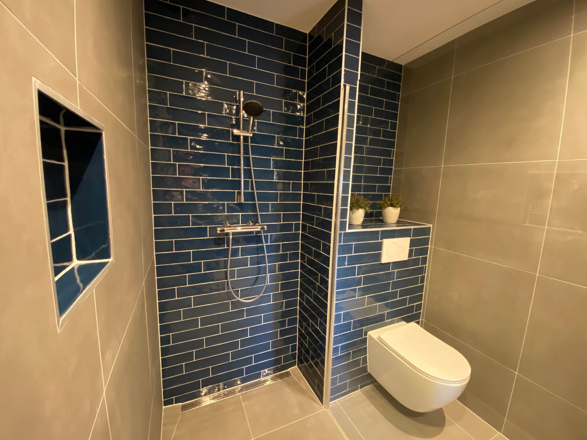 Moderne badkamer met donkerblauwe tegels,  inloopdouche . Toilet , badkamermeubel en een staand handdoekenrek. 