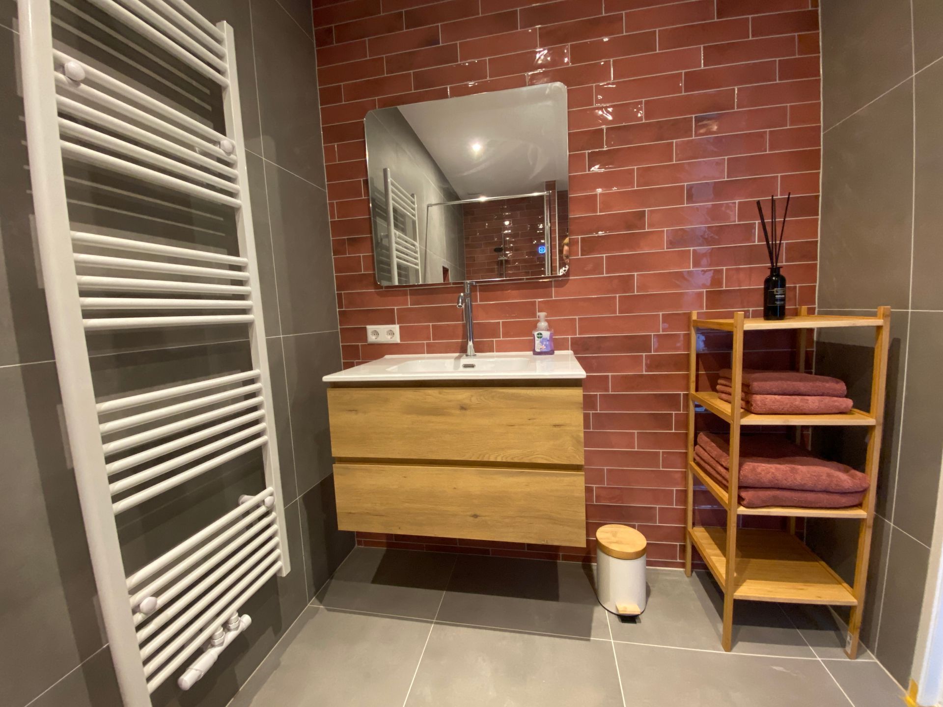 Moderne badkamer met een roze tegemuur, zwevend houten badmeubel, spiegel, handdoekradiator en opbergrek.