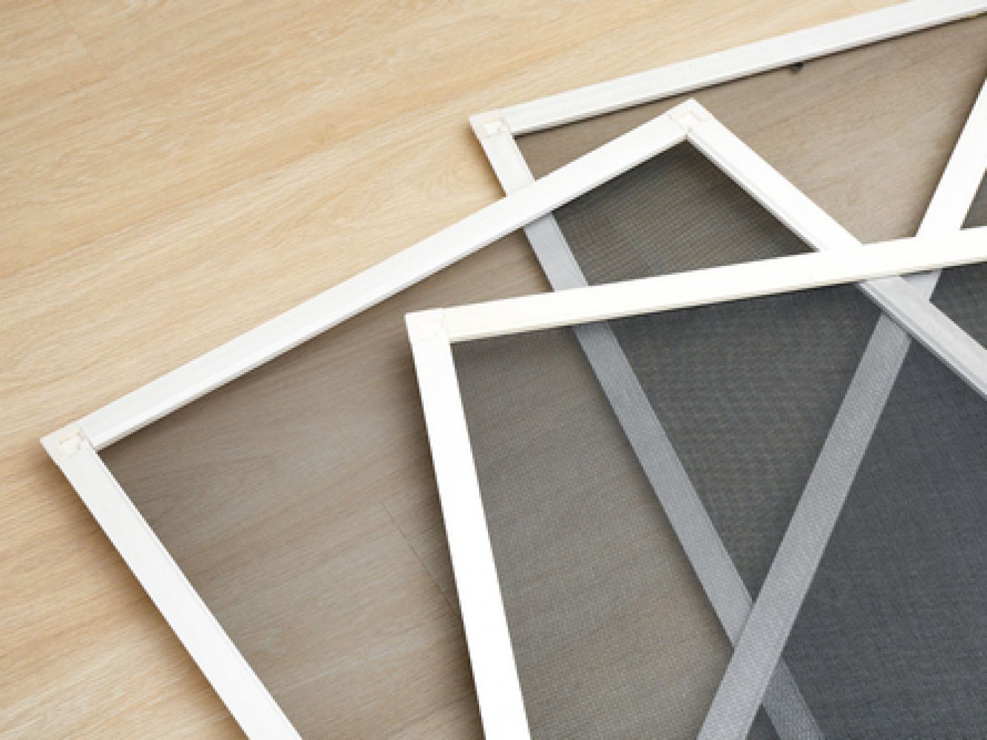 Three rectangular window screens with white frames on a light wood surface.