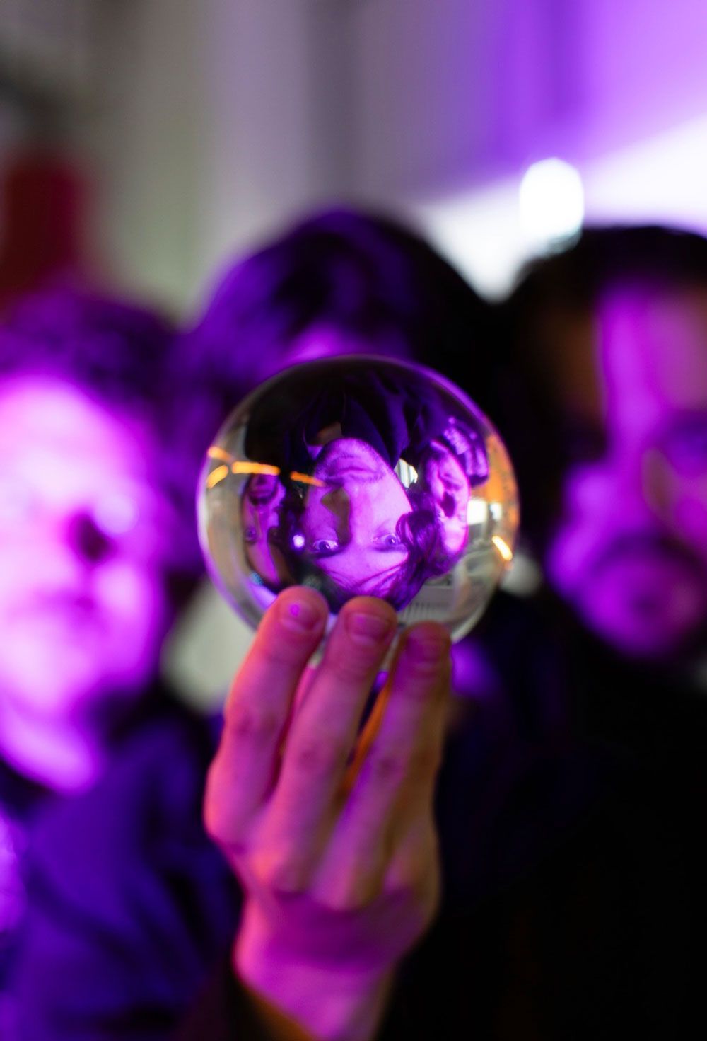 Hand holding a clear glass sphere reflecting three people under purple lighting