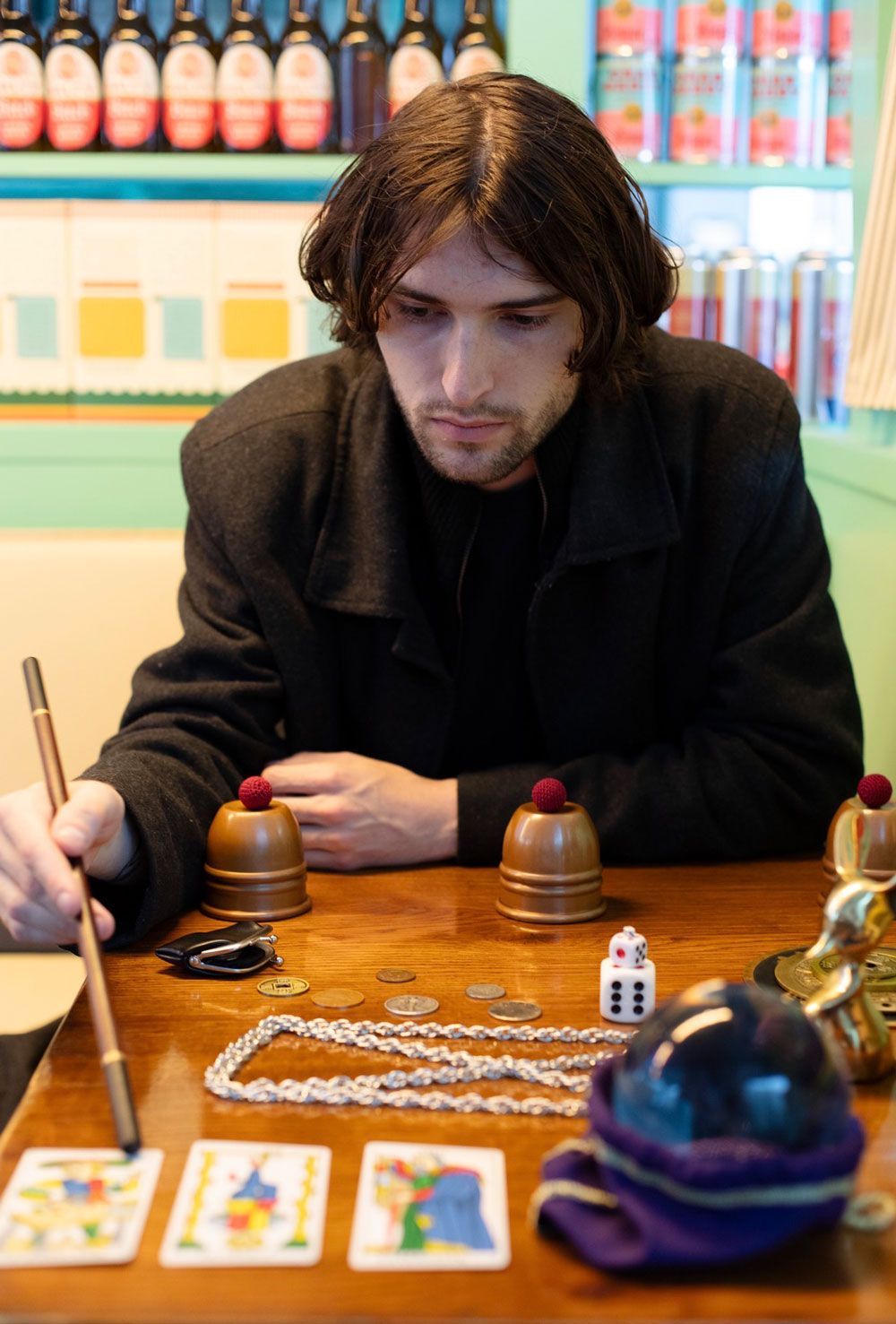 Person leaning over a wooden table with game pieces and cards in a brightly lit shop or arcade.