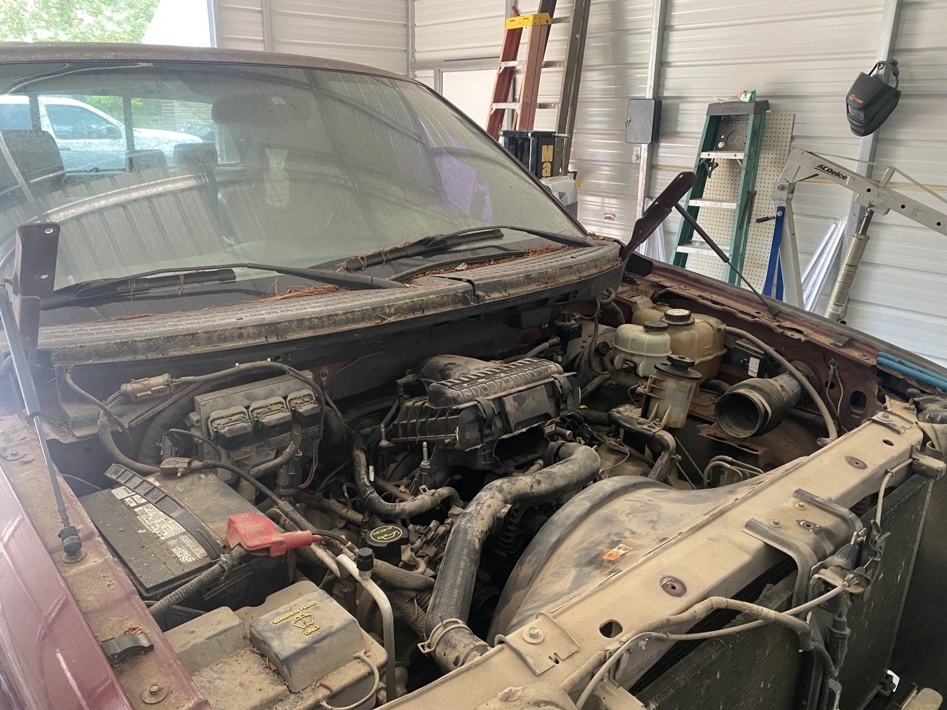 A dirty truck with the hood open is sitting in a garage.