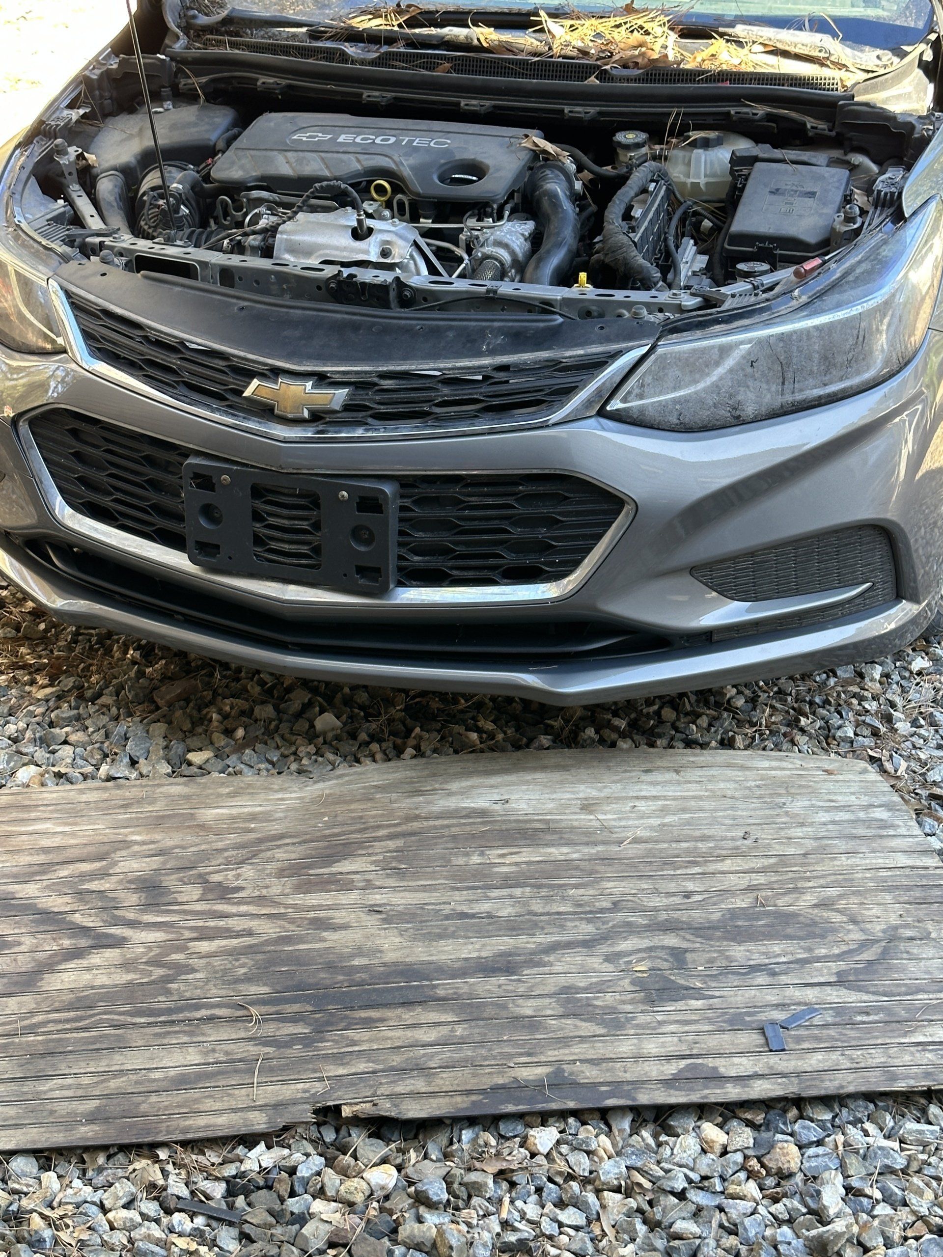 A gray car with the hood up is sitting on a wooden board.