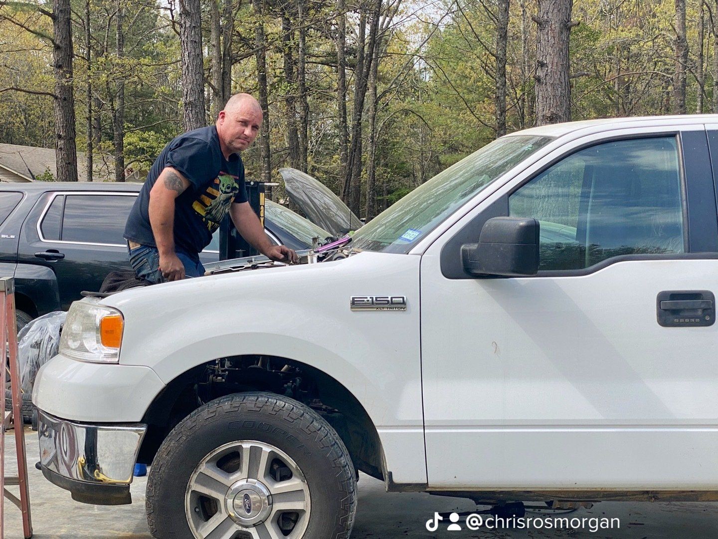 A man is working on the hood of a white truck.