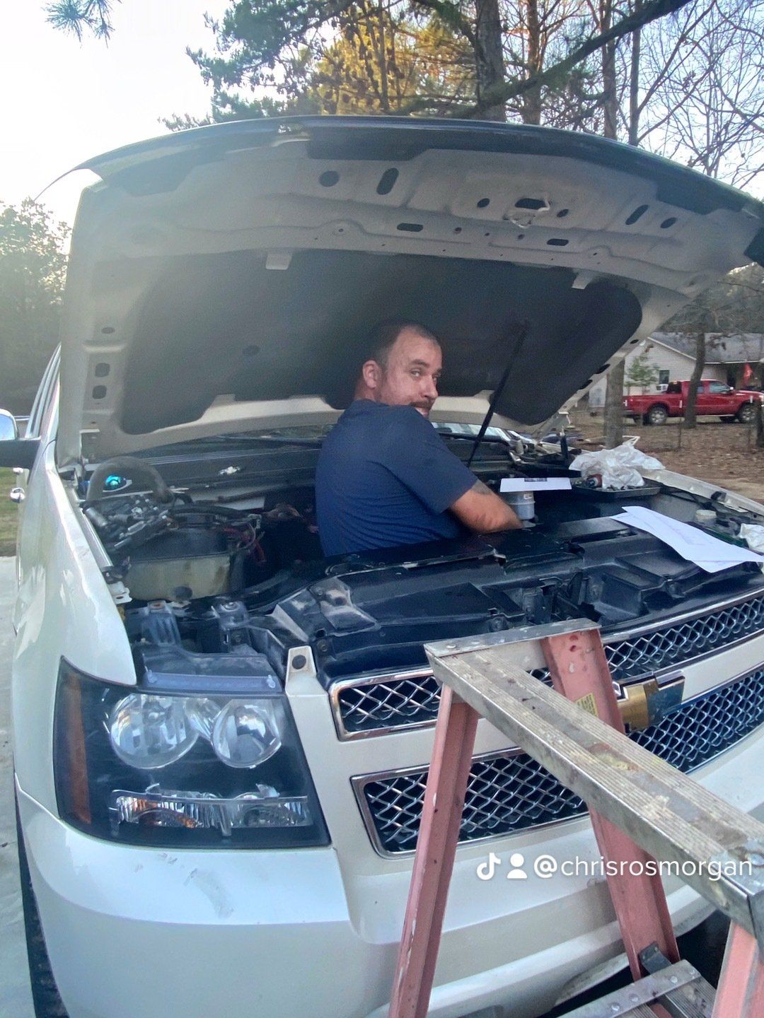 A man is sitting under the hood of a white suv.