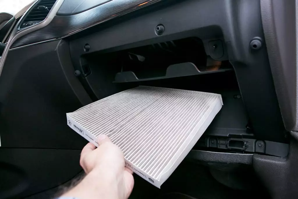A person is taking a air filter out of the glove box of a car.