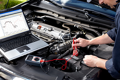 A man is working on the engine of a car with a laptop.