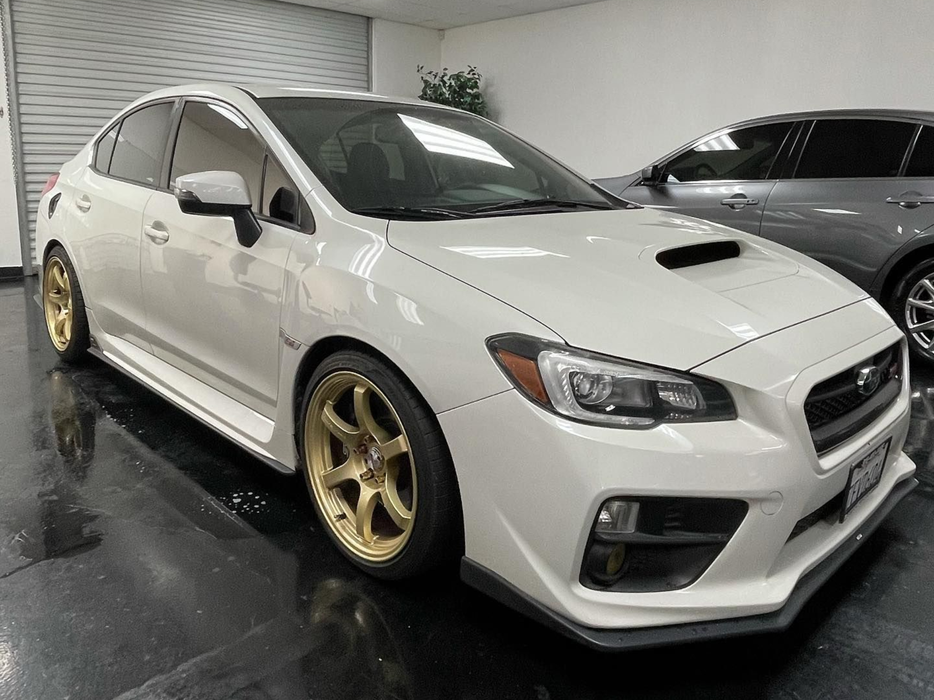 A white subaru wrx sti with gold wheels is parked in a garage.