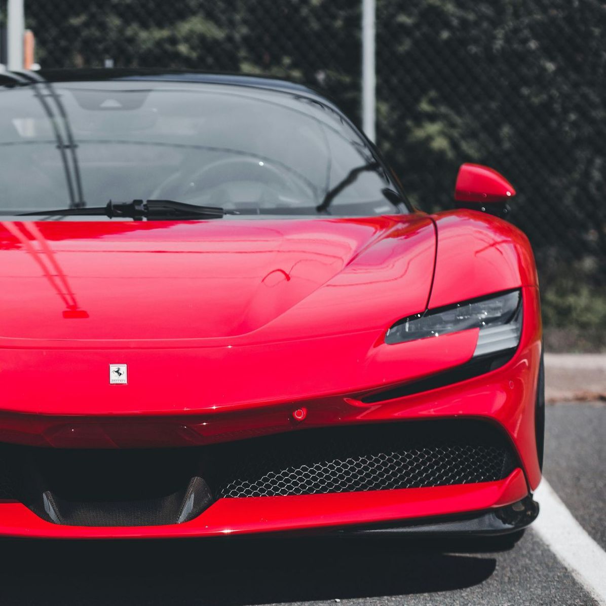 Red Ferrari sports car parked on asphalt, front view. Black roof, black grille, and a white logo.