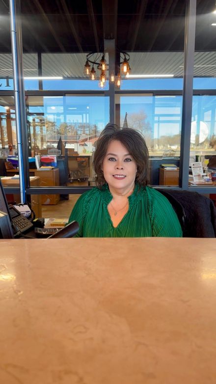 Woman seated at a table in a bright café with large windows and hanging lights.