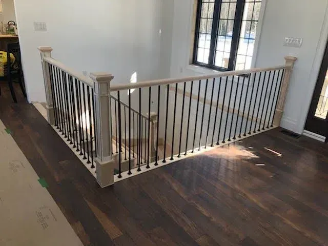 Stair landing with white railings, dark wood floor, and large windows in a bright interior.