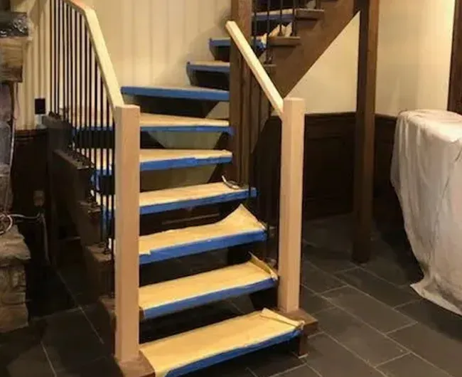 Partially assembled wooden staircase with blue-taped steps in an indoor room