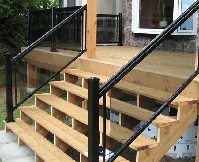 Wooden outdoor staircase with black railings beside a house deck.