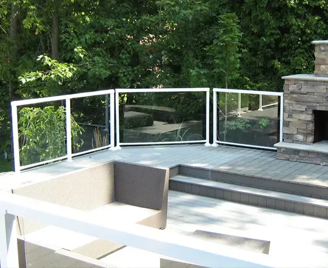 Modern outdoor patio with white railing, steps, and stone fireplace overlooking trees