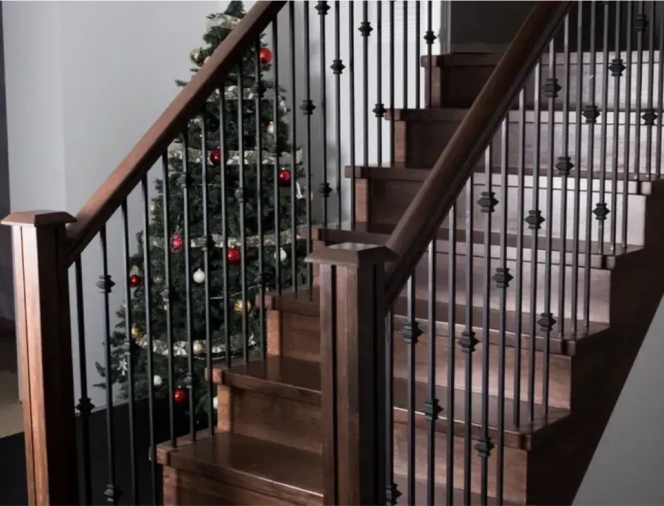 Staircase with dark wood railings and black balusters beside a decorated Christmas tree