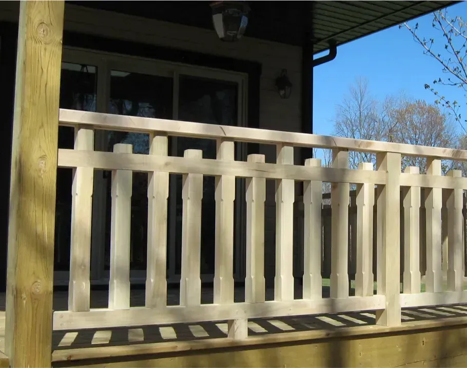 Beige porch railing in front of a house with a shaded doorway and blue sky beyond
