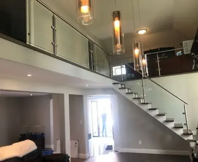 Modern loft interior with staircase, glass railing, pendant lights, and high ceilings